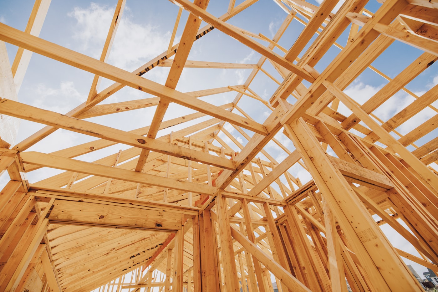 New timber roof trusses, top plates and studs seen looking up from inside an unclad frame, blue sky between the members